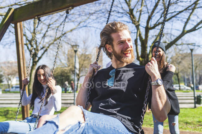 Cheerful friends swinging in park during sunny day — Stock Photo