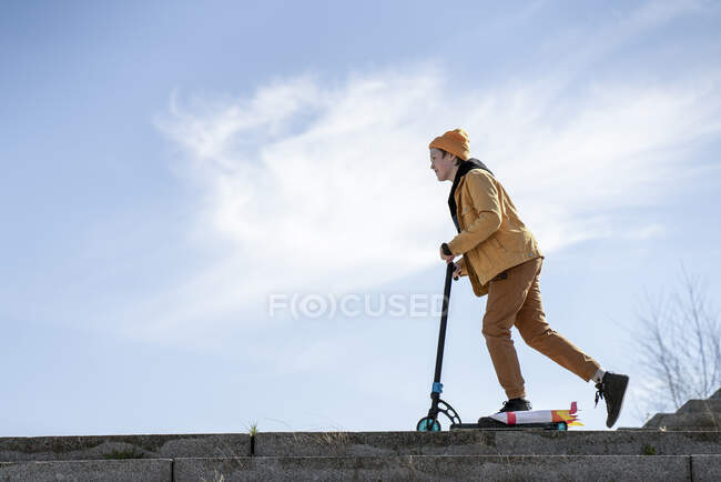 Garçon équitation pousser scooter sur les marches contre le ciel bleu — Photo de stock