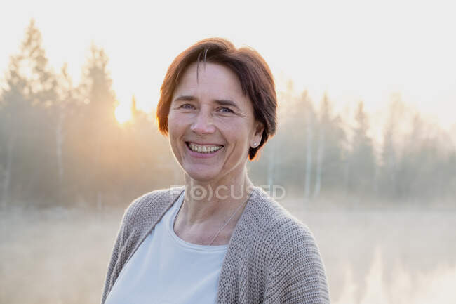 Porträt einer erwachsenen Frau, die bei nebligem Sonnenaufgang in die Kamera lächelt — Stockfoto