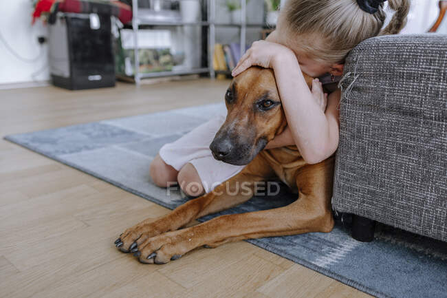 Mädchen umarmt Hund beim Entspannen auf Teppich im heimischen Wohnzimmer — Stockfoto