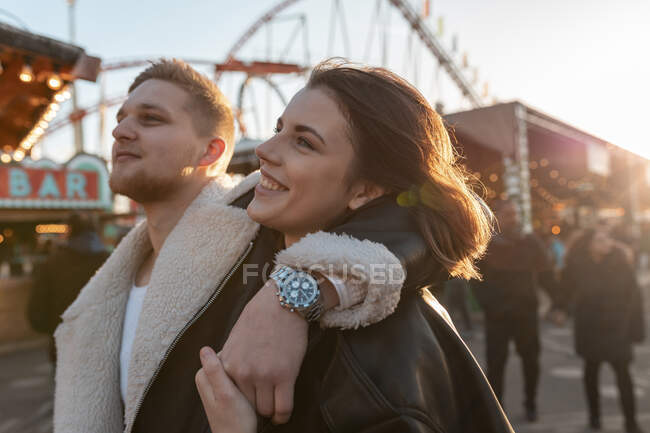 Крупним планом молодий чоловік з рукою на плечі дівчини, стоячи в парку розваг на заході сонця — стокове фото