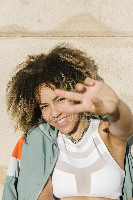 Щаслива молода жінка жестикулює знак миру під час сонячного дня — стокове фото