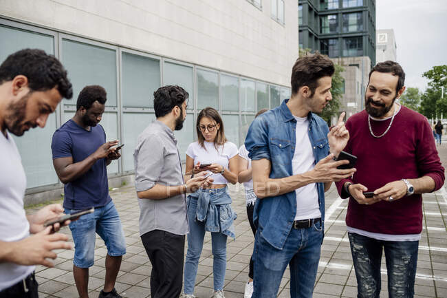 Freunde reden und nutzen Smartphones, während sie auf Fußweg in der Stadt stehen — Stockfoto