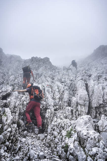 Male hikers climbing on rocky mountain against sky during foggy weather, Bergamasque Alps, Italy — Stock Photo