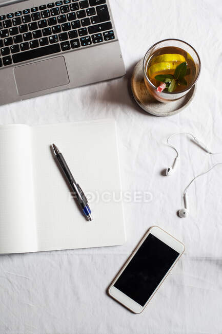 Mobile phone with book and tea by laptop on desk in office — Stock Photo
