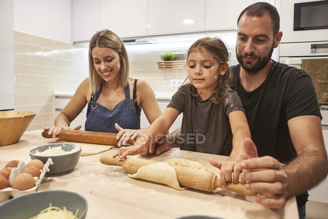 Genitori con figlia impastando la pasta di pizza sul tavolo in cucina — Foto stock