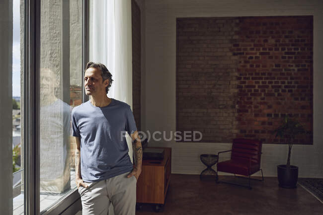 Senior man looking out of window in a loft flat stock photo