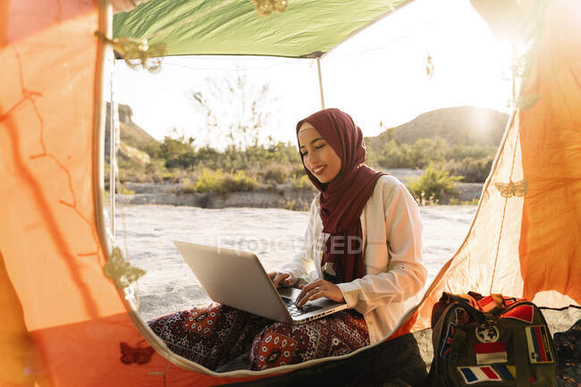 Mujer joven usando Hijab usando portátil en una tienda de campaña - foto de stock