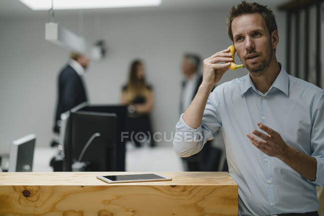 Uomo d'affari in piedi in ufficio porta aperta, utilizzando banana come telefono — Foto stock