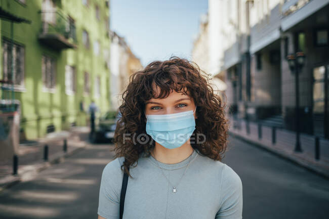 Brünette lockige Frau mit Schutzmaske in der Stadt — Stockfoto