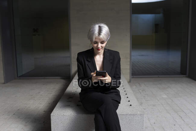 Женщина-профессионал в элегантном костюме с помощью смартфона, сидя в офисе — стоковое фото
