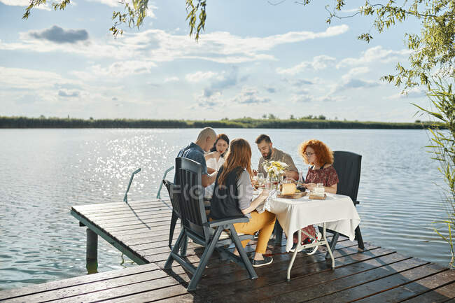 Amis dînant sur une jetée près d'un lac — Photo de stock
