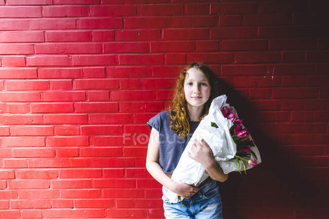 Girl holding bouquet while standing against red wall in city — Stock Photo