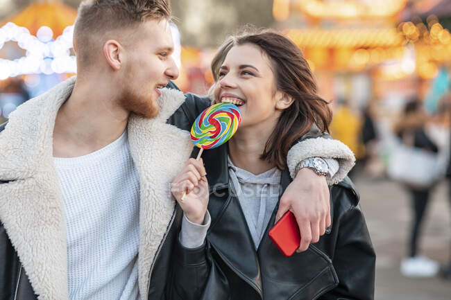 Happy woman looking at boyfriend while eating lollipop at amusement park — Stock Photo