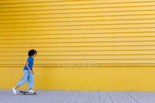 Молодая женщина катается на скейтборде перед желтой стеной — стоковое фото