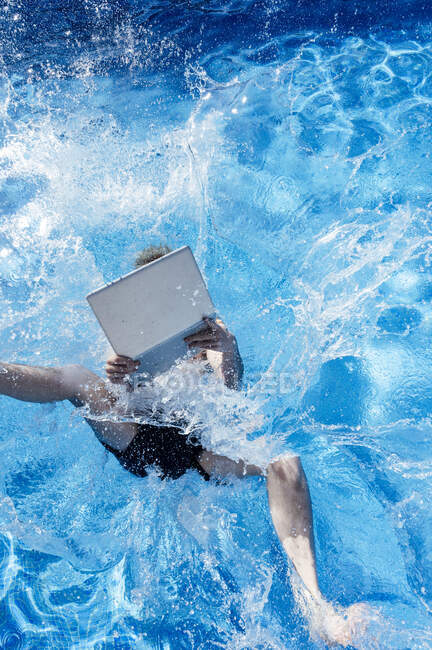 Jovem com laptop caindo na piscina durante o dia ensolarado — Fotografia de Stock