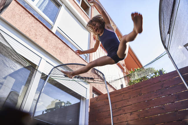 Fille gaie sautant sur trampoline contre la maison pendant la journée ensoleillée — Photo de stock