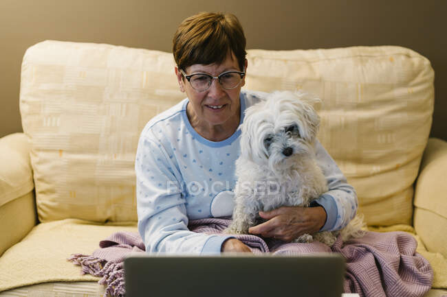 Ill mulher sênior sentado com o cão enquanto discute sobre chamada de vídeo através de laptop em casa — Fotografia de Stock