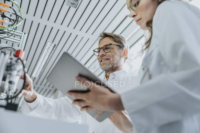 Jovem mulher usando tablet digital enquanto colega masculino examinando máquinas na fábrica — Fotografia de Stock