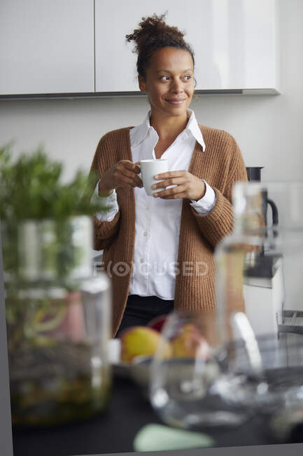 Ritratto di donna d'affari sorridente in piedi in cucina con tazza di caffè guardando a distanza — Foto stock
