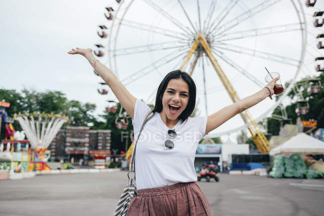 Carefree young woman with arms raised standing at amusement park — Stock Photo