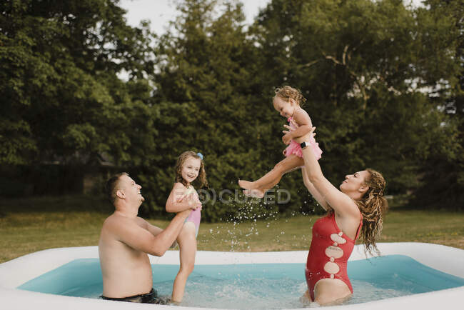 Familia feliz jugando en una piscina inflable en el jardín - foto de stock