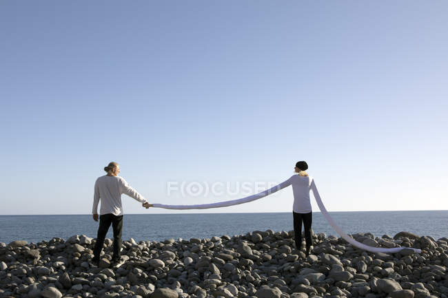 Donna con lunghe braccia che tiene la mano dell'uomo in spiaggia contro il cielo limpido — Foto stock