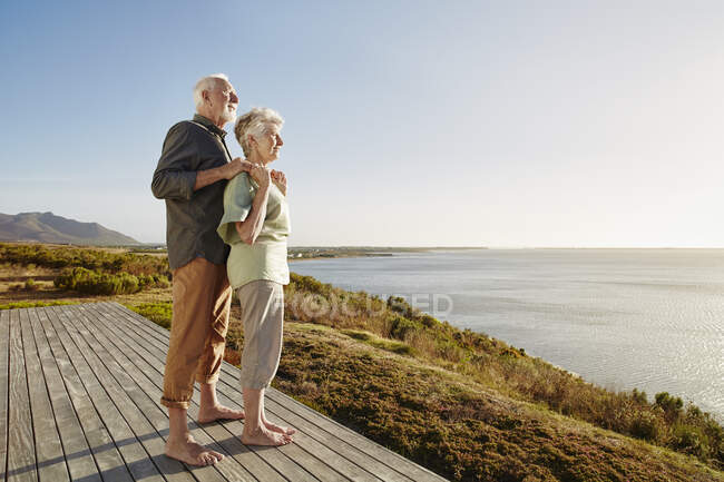 Seniorenpaar genießt Aussicht auf Holzterrasse am Meer — Stockfoto