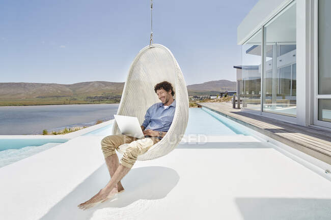 Чоловік сидить у висячому кріслі над басейном за допомогою ноутбука — стокове фото
