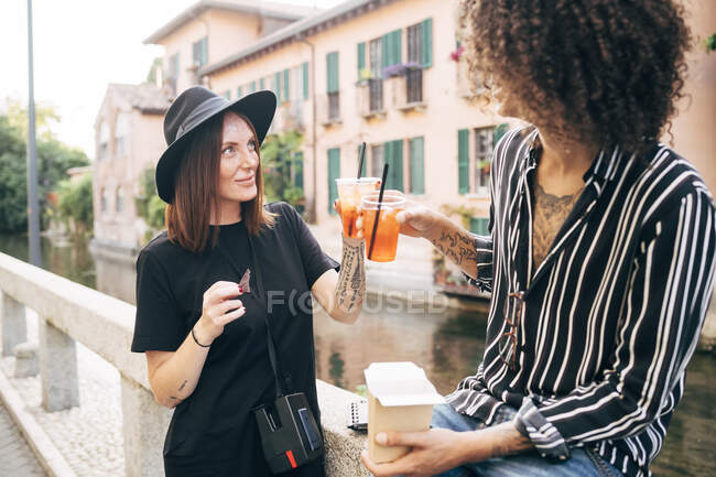 Человек тост напиток с подругой, сидя на сохраняющей стене в городе — стоковое фото