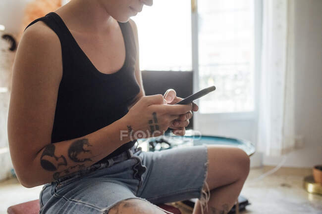 Mulher usando telefone inteligente enquanto sentado na sala de estar — Fotografia de Stock