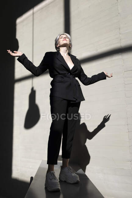 Professionista donna che indossa abito elegante in piedi sulla parete di sostegno con luce solare e ombra sullo sfondo — Foto stock
