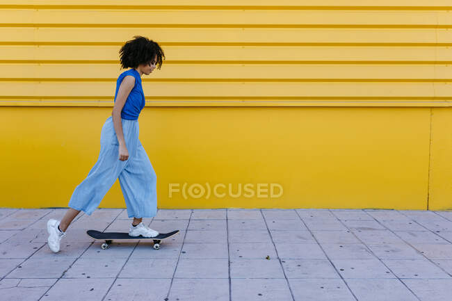 Giovane donna skateboard davanti al muro giallo — Foto stock