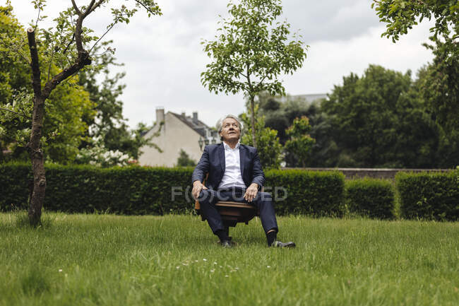 Старший бізнесмен сидить на стільці в сільському садку, дивлячись вгору — стокове фото