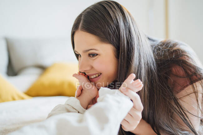 Feliz madre sosteniendo las piernas del bebé en el dormitorio - foto de stock
