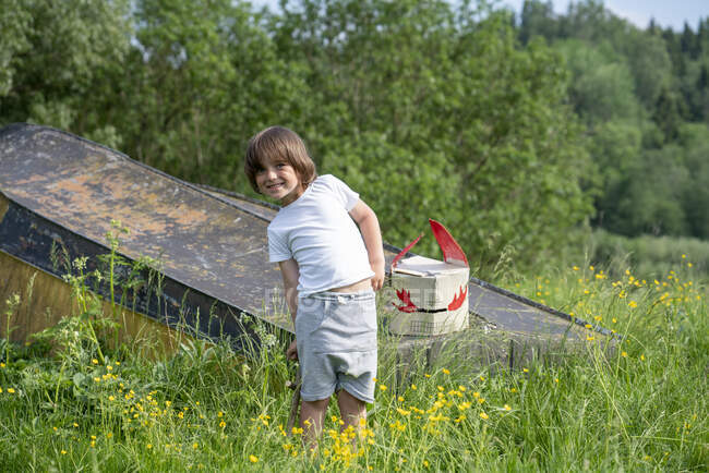Smiling boy with mask on abandoned boat standing amidst plants in forest — Stock Photo