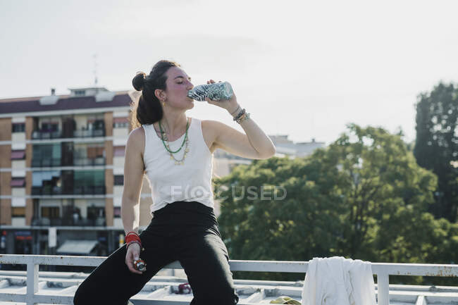 Woman drinking water while sitting on railing outdoors — Stock Photo