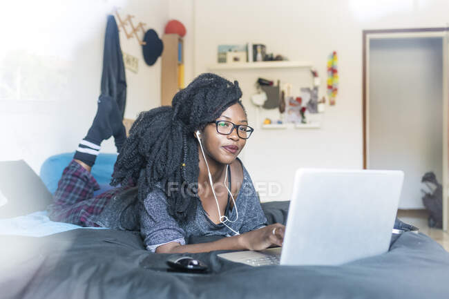 Jeune femme utilisant un ordinateur portable sur le lit à la maison — Photo de stock