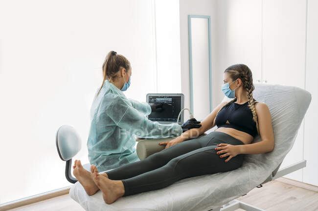 Medico indossando maschera viso esaminando sportiva con scanner ad ultrasuoni — Foto stock