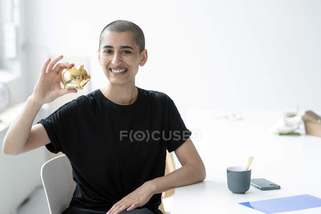 Портрет улыбающейся женщины, держащей золотую копилку за столом в офисе — стоковое фото