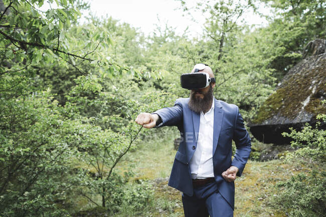 Homme d'affaires pratiquant les arts martiaux tout en regardant à travers simulateur de réalité virtuelle contre les arbres dans la forêt — Photo de stock