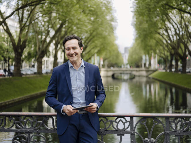 Porträt eines glücklichen reifen Geschäftsmannes, der mit Tablet auf einer Brücke steht — Stockfoto