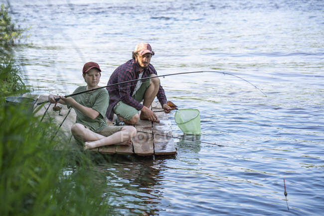 Vater und Sohn angeln im Fluss, während sie auf der Promenade sitzen — Stockfoto