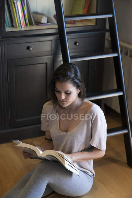 Женщина читает книгу, сидя дома на полу — стоковое фото
