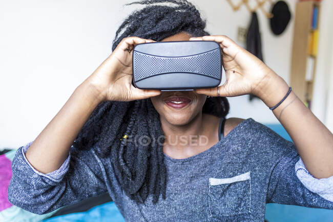 Young woman using virtual reality glasses sitting on bed — Stock Photo