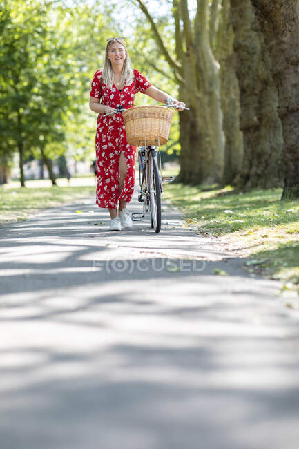 Щаслива жінка їздить велосипедом по доріжці в громадському парку в сонячний день. — стокове фото