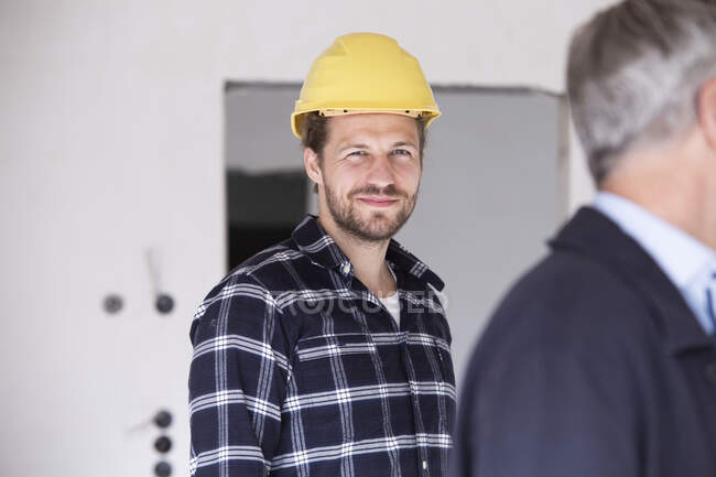 Operaio edile sorridente in piedi con l'architetto nella costruzione di casa — Foto stock