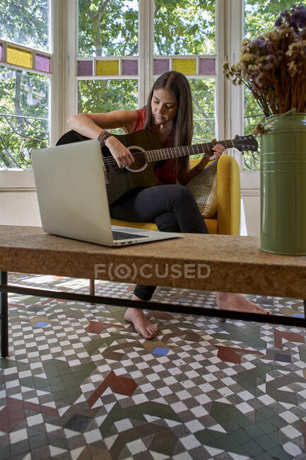 Donna che impara la chitarra online mentre siede sulla sedia in salotto — Foto stock
