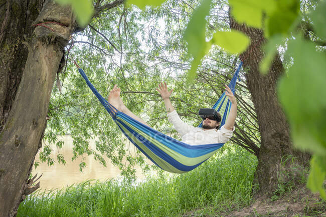 Man with 3d glasses relaxing on hammock at riverside — Stock Photo