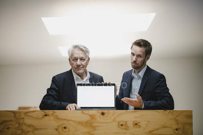 Два уверенных бизнесмена сидят в офисе, представляя экран ноутбука, улыбаясь — стоковое фото